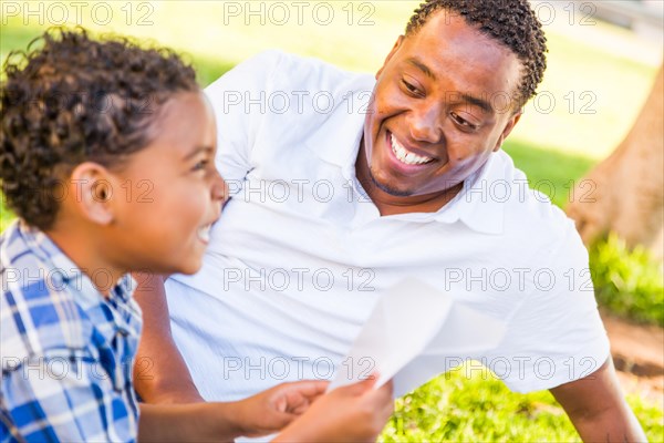 Happy african american father and mixed-race son playing with paper airplanes in the park