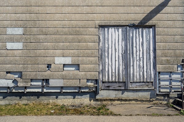 Altes Fabrikgebaeude mit beschaedigter Wand und vergammelter Brettertuer