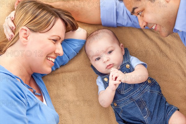 Young mixed-race couple laying with their infant on A blanket