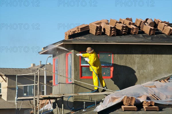 Construction worker pressure washes fresh applied surface of new home exterior