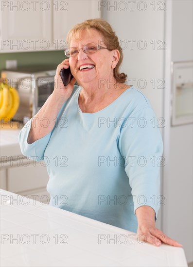 Happy senior adult woman on her smart cell phone in kitchen