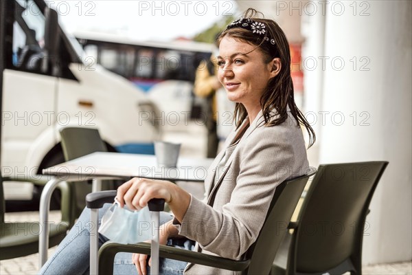 A young traveler with the luggage and protective mask sitting in the cafe and waiting for her bus to come