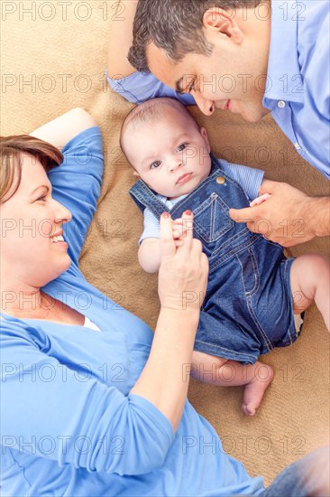 Young mixed-race couple laying with their infant on A blanket