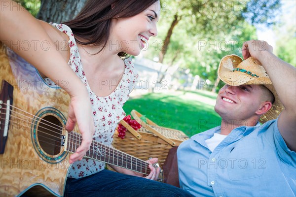 Young adult girl playing guitar with boyfriend in the park