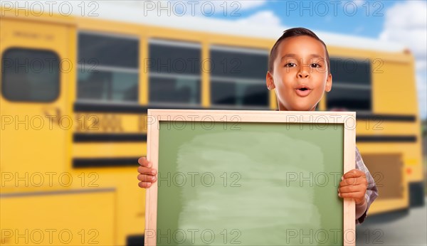 Young hispanic boy with blank chalkboard near school bus