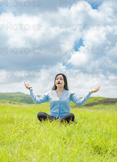 Young woman doing yoga on the grass in the field with blue sky in the background