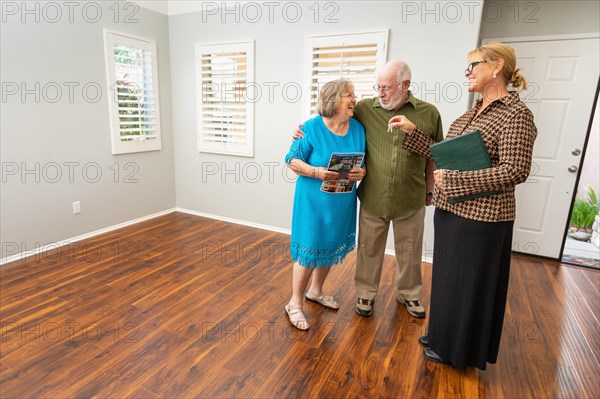 Female real estate agent handing new house keys to senior adult couple in new home