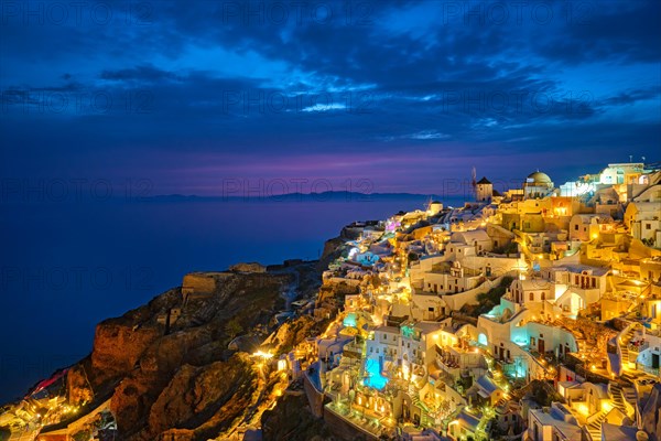 Famous greek iconic selfie spot tourist destination Oia village with traditional white houses and windmills in Santorini island in the evening blue hour