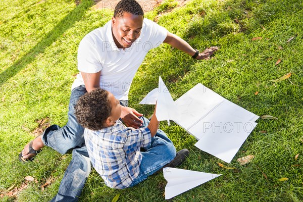 Happy african american father and mixed-race son playing with paper airplanes in the park