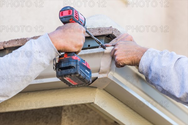 Workers attaching aluminum rain gutter to fascia of house