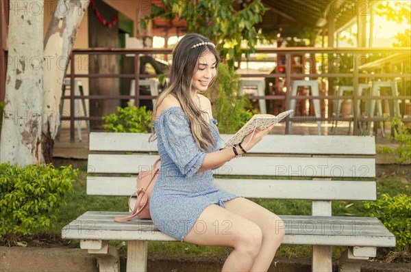 A cute girl sitting on a bench reading a book