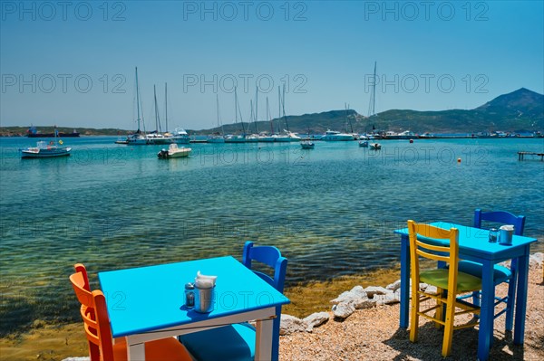 Cafe restaurant table of street cafe with chairs on beach in Adamantas town on Milos island with Aegean sea with boats and yachts in background. Milos island