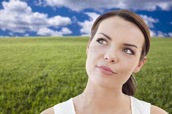 Contemplative woman in grass field looking up and over to the side