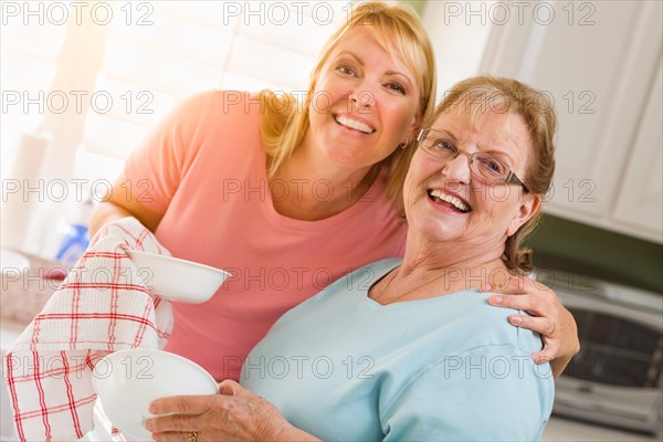 Portrait of smiling senior adult woman and young daughter at sink in kitchen