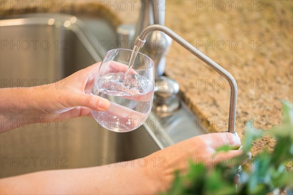 Woman pouring fresh reverse osmosis purified water into glass in kitchen