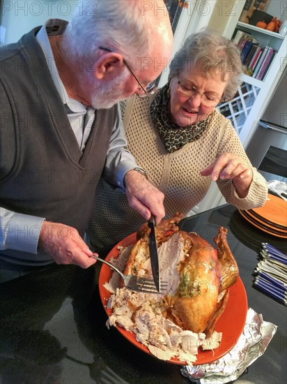 Senior adult couple cutting the holiday Turkey together in the kitchen