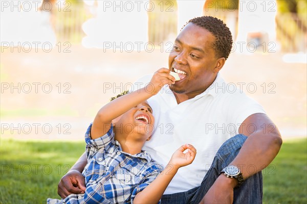 African american father and mixed-race son eating an apple in the park