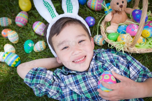 mixed-race chinese and caucasian boy outside wearing rabbit ears playing with easter eggs