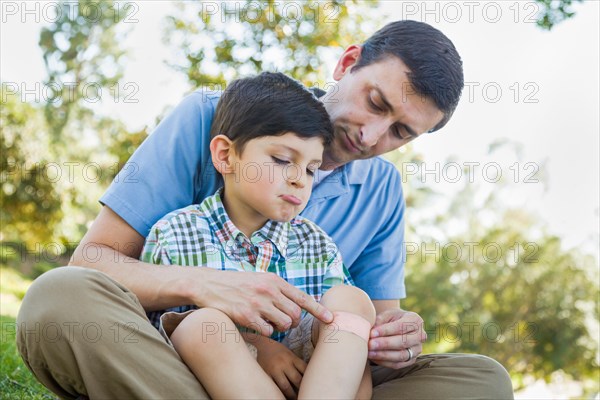 Loving father puts a bandage on the elbow of his young son in the park