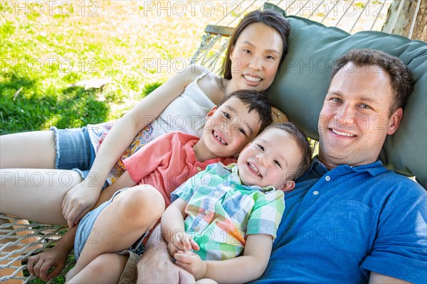 Caucasian father and chinese mother relaxing in hammock with mixed-race sons