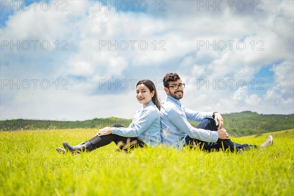 A wedding couple sitting with their backs to each other on the grass