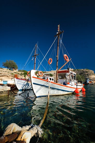 Fishing boats moored in crystal clear turquoise sea water in harbour in Greek fishing village of Mandrakia