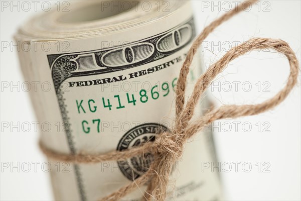 Roll of one hundred dollar bills tied in burlap string on white