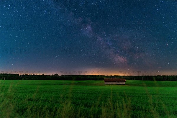 Milky Way over a nocturnal green field with a solitary barn