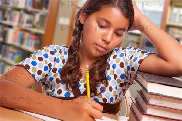 Hispanic girl student with pencil and books studying in library