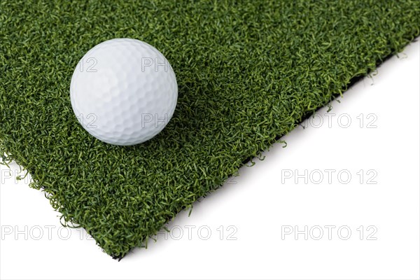 Golf ball resting on section of artificial turf grass on white background