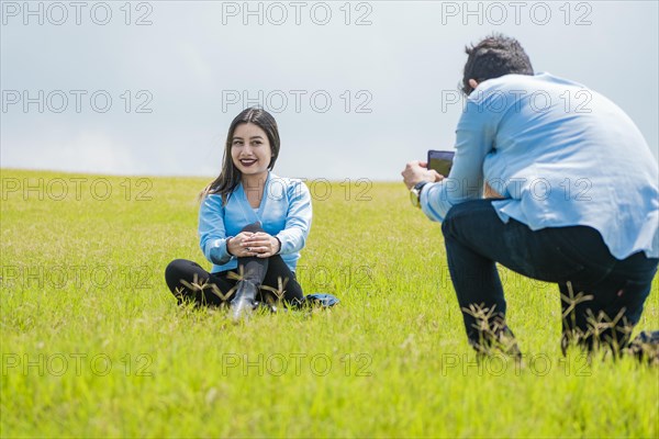 A guy taking a picture of a girl in the field