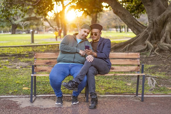 Gay Latino male couple sitting on a bench in a park at sunset