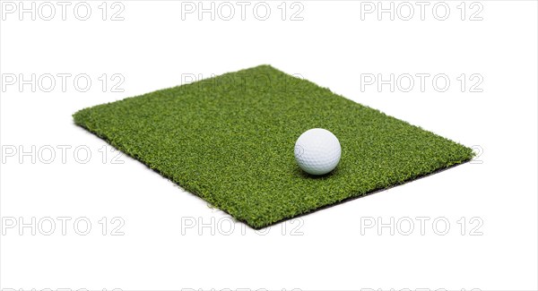 Golf ball resting on section of artificial turf grass on white background