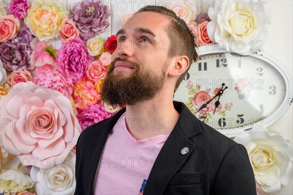 Portrait eines jungen Mannes mit langem Vollbart und kurzen Haaren bekleidet mit einem schwarzen Sakko und einem rosa Shirt. Sein Blick richtet sich hoffnungsvoll nach oben