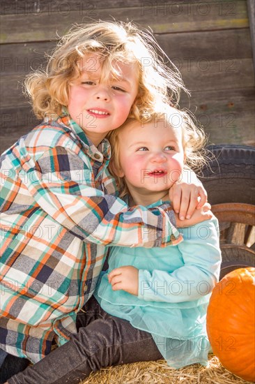 Sweet little boy plays with his baby sister in a rustic ranch setting at the pumpkin patch