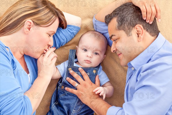 Young mixed-race couple laying with their infant on A blanket