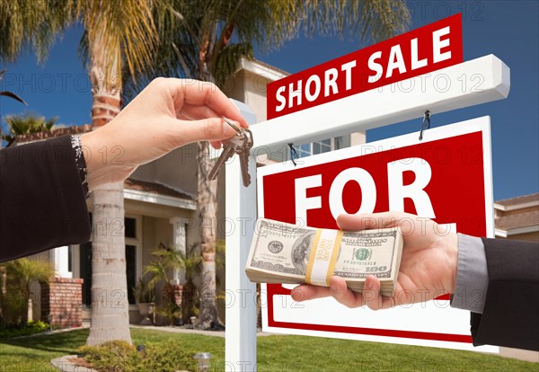 Handing over cash for house keys and short sale real estate sign in front of home