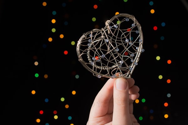 Heart shaped metal cage in hand on bokeh light background