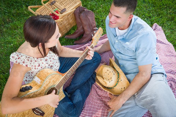 Young adult girl playing guitar with boyfriend in the park