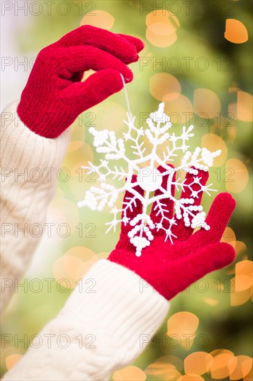 Woman wearing seasonal red mittens holding white snowflake christmas ornament
