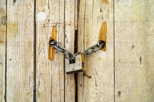 Rusty padlock locking old wooden door with a chain