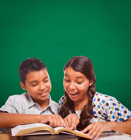 Blank chalk board behind hispanic boy and girl having fun studying together