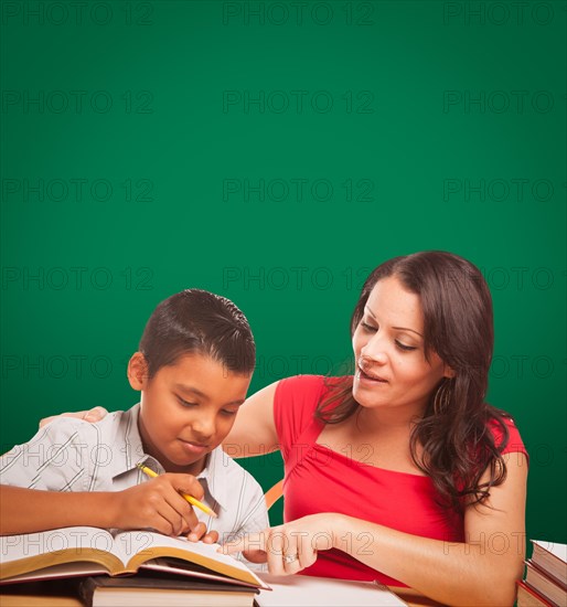 Blank chalk board behind hispanic young boy and famale adult studying