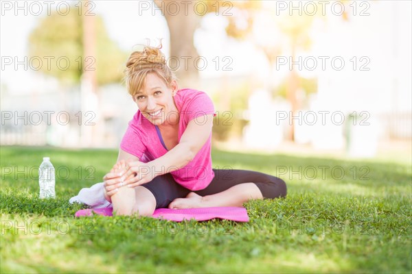 Young fit flexible adult woman outdoors on the grass with yoga mat stretching her legs