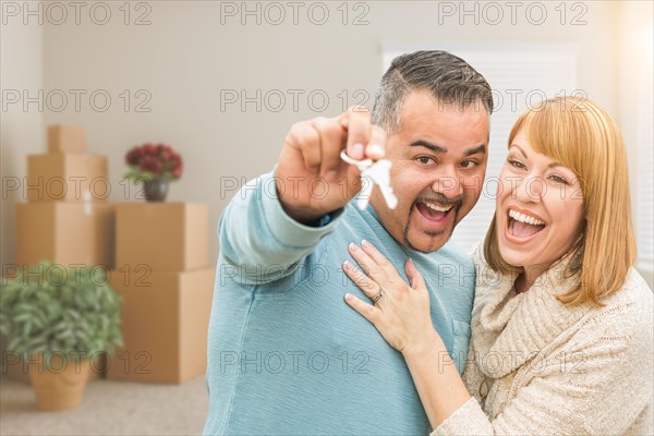 mixed-race couple holding house keys inside empty room with moving boxes