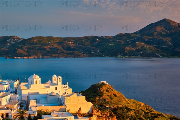 View of Plaka village on Milos island with traditional greek white houses with Greek Orthodox christian churck on sunset. Plaka town