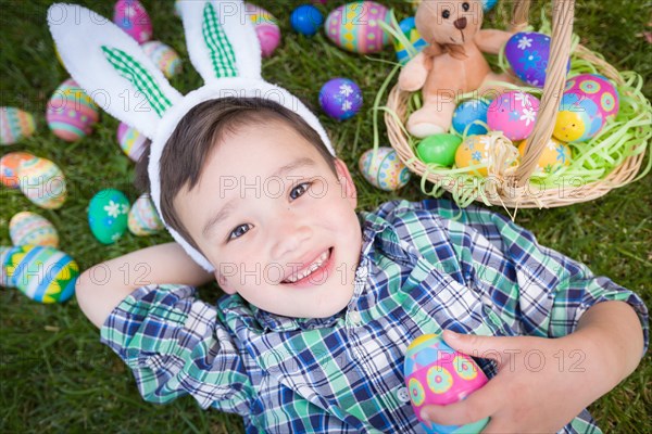 mixed-race chinese and caucasian boy outside wearing rabbit ears playing with easter eggs