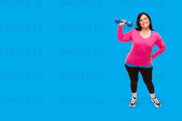 Middle aged hispanic woman in workout clothes holding dumbbell against A bright cyan blue background