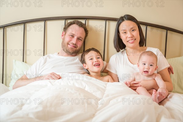 Young mixed-race chinese and caucasian baby boys laying in bed with their father and mother