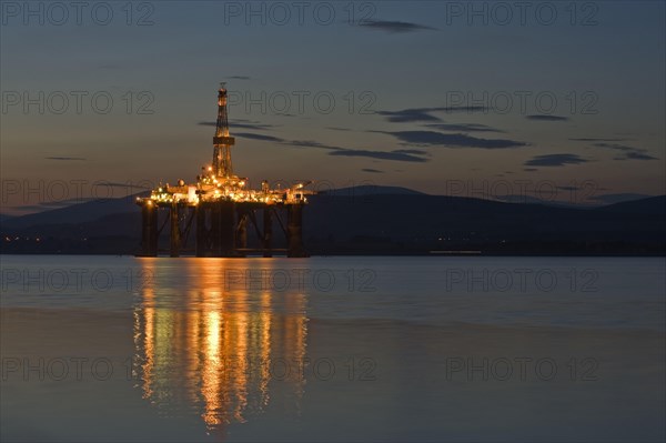 Oil rig moored in sea near coast at night